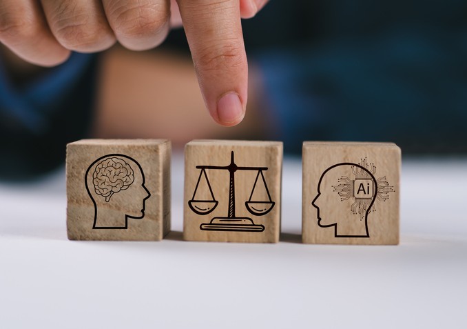 Hand die naar drie houten blokjes wijst met daarop een menselijk brein, een weegschaal en een AI-hoofd, als symbool voor de balans tussen mens, recht en kunstmatige intelligentie.