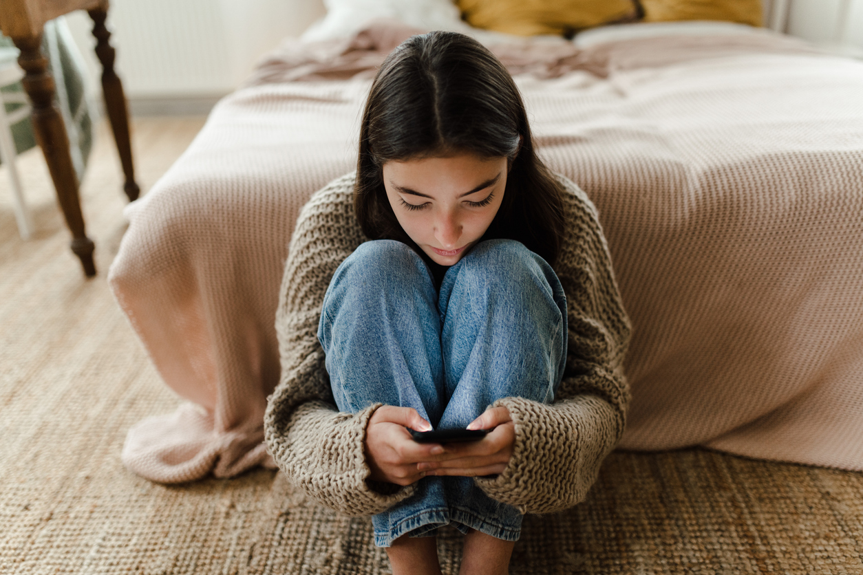 meisje zit op de grond tegen bed aan op de mobiele telefoon